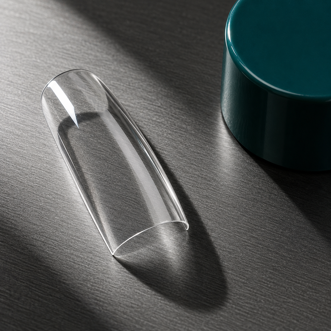 Close-up of a sculpted clear nail tip on a dark surface